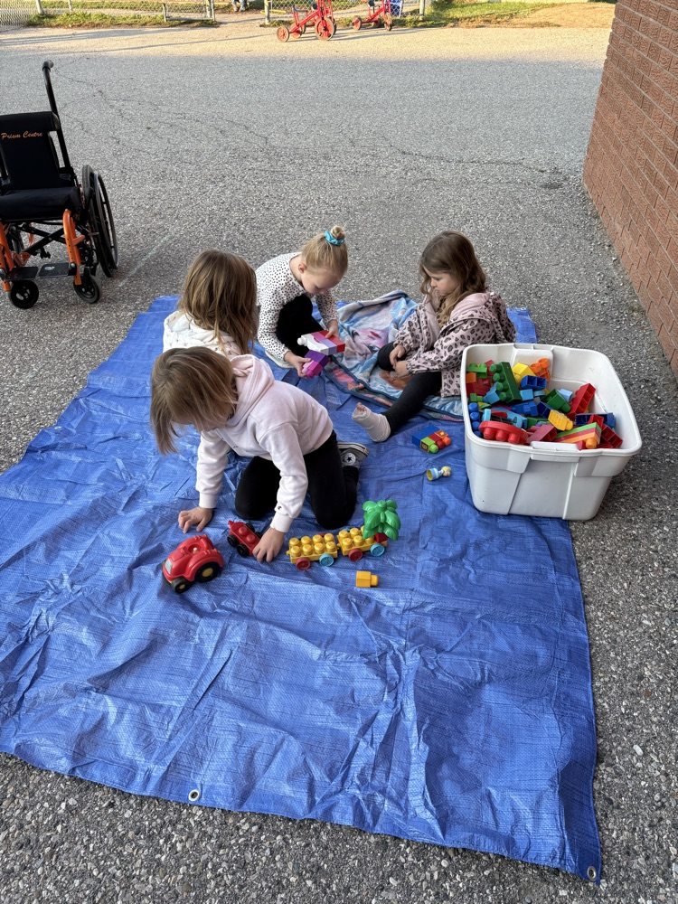 Kindergarten students sitting outside on a green tarp learning together