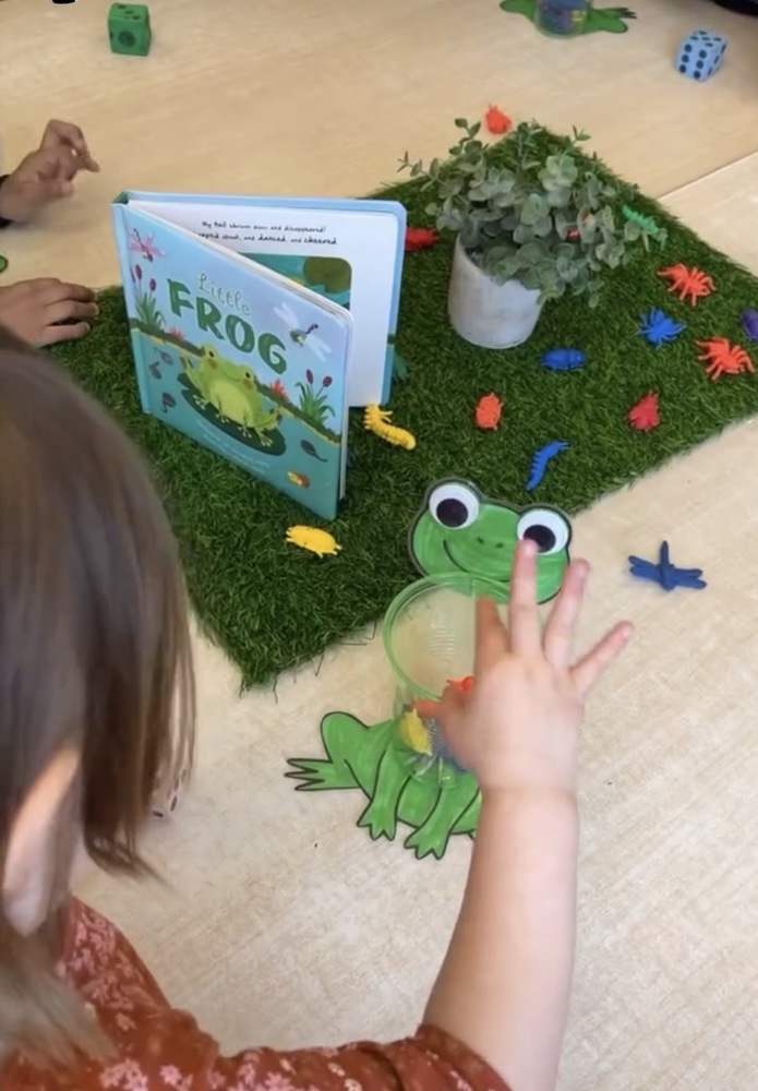 A child counting with a frog, frog book, and dragonfiles.