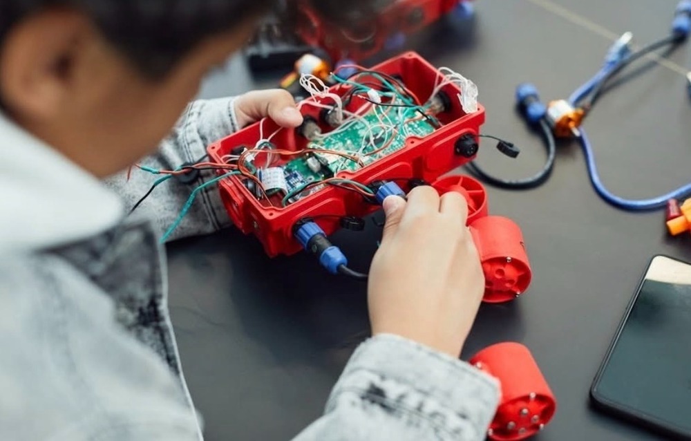 A child working on a STEM project with wires, cords, and plugs. 