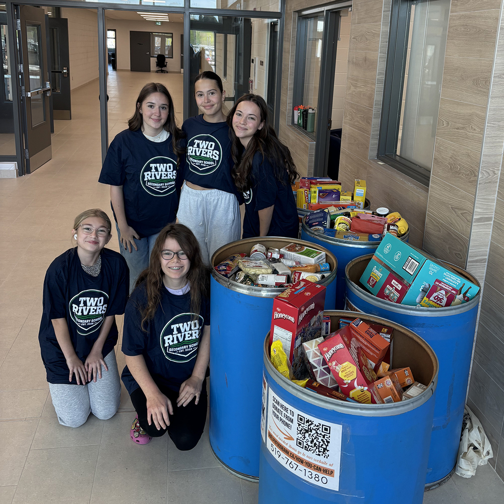 Students pose for a photo next to full bins of food donations.