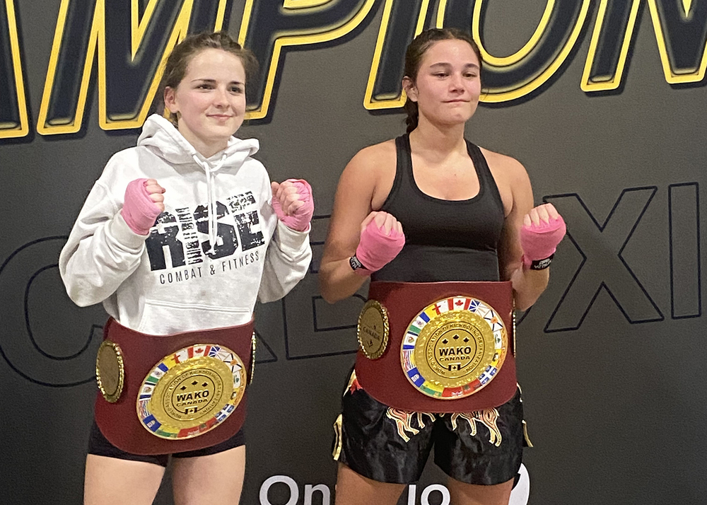 2 kickboxing athletes pose for a photo wearing championship belts.