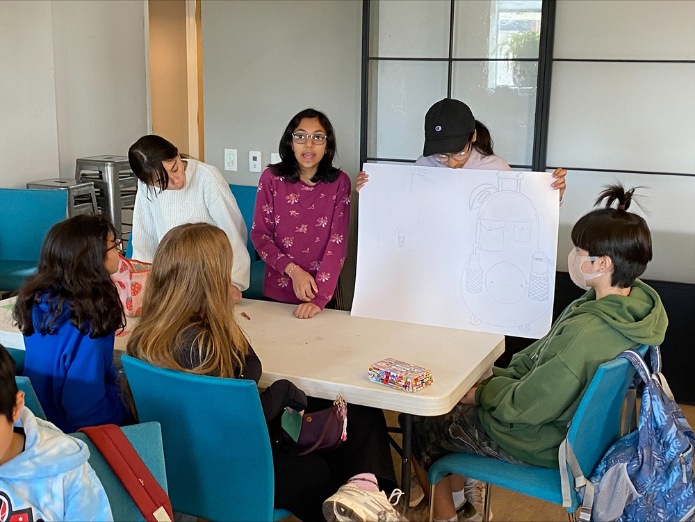 A group of students sit around a work table, looking at a poster board.
