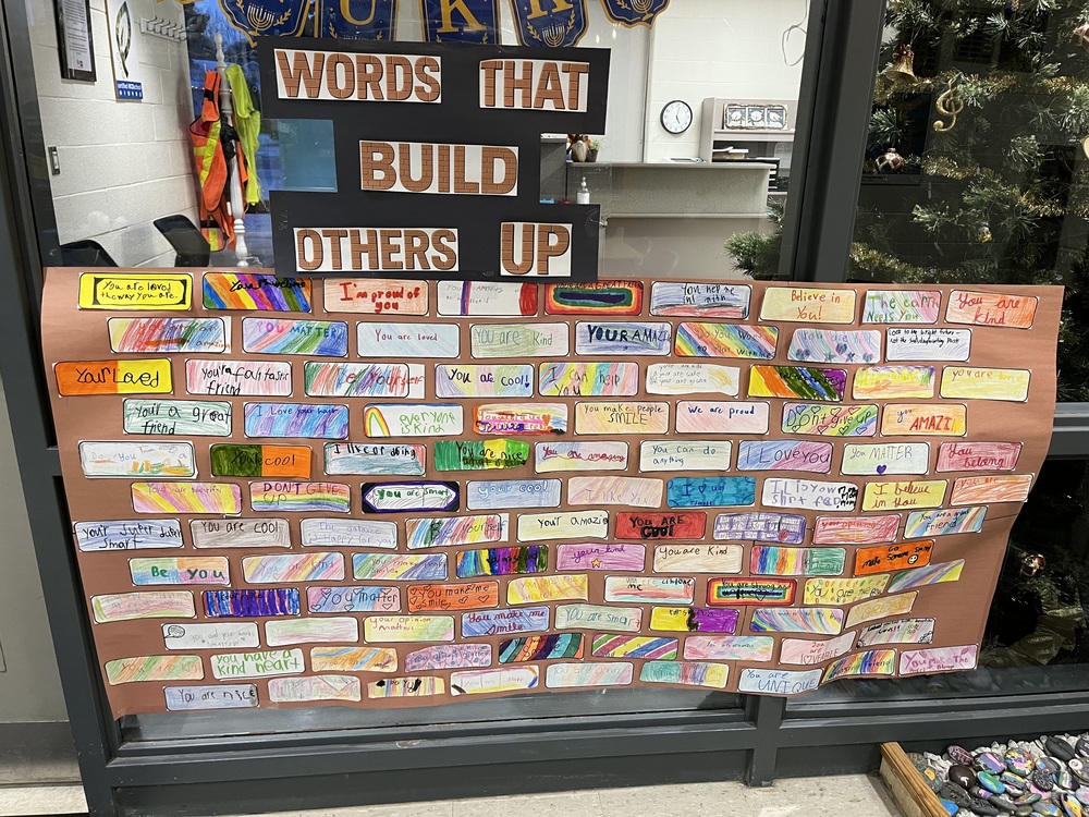 small paper bricks with words that make people feel good, they are put together to look like a brick wall on brown paper with the words, "Words that Build Others Up"