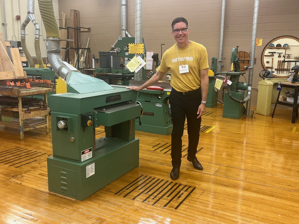 A man stands next to shop equipment in a school tech room.