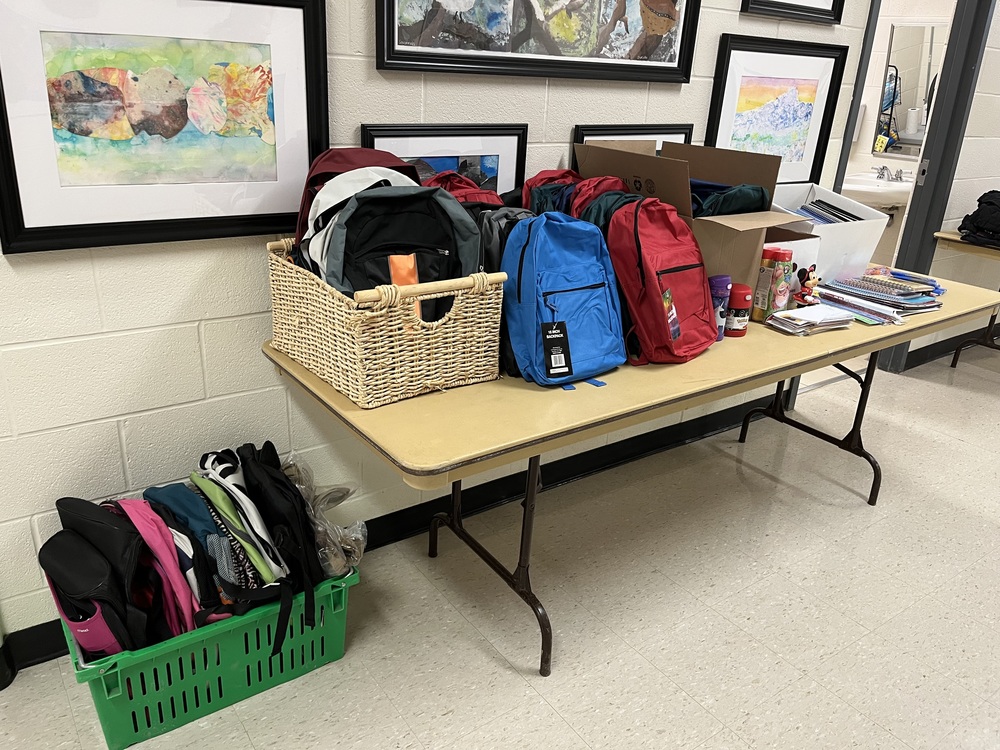backspacks in lots of colours and school supplies (notebooks, crayons) laid out on a table.