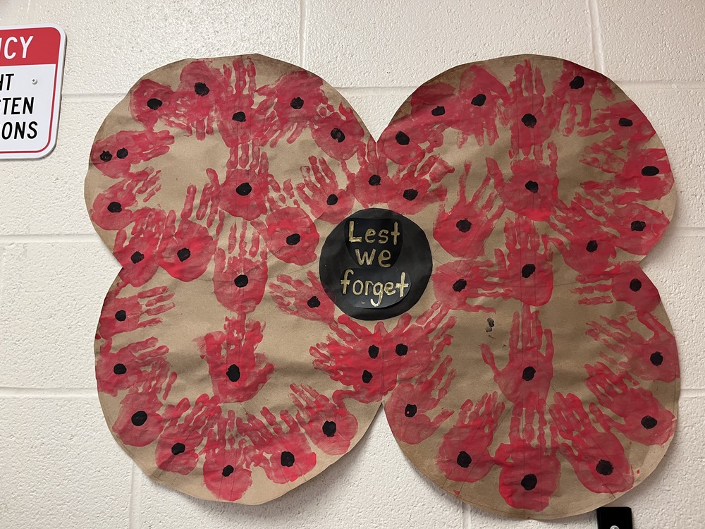 A large poppie with Lest We Forget in the black circle middle with red children's  handprints. 