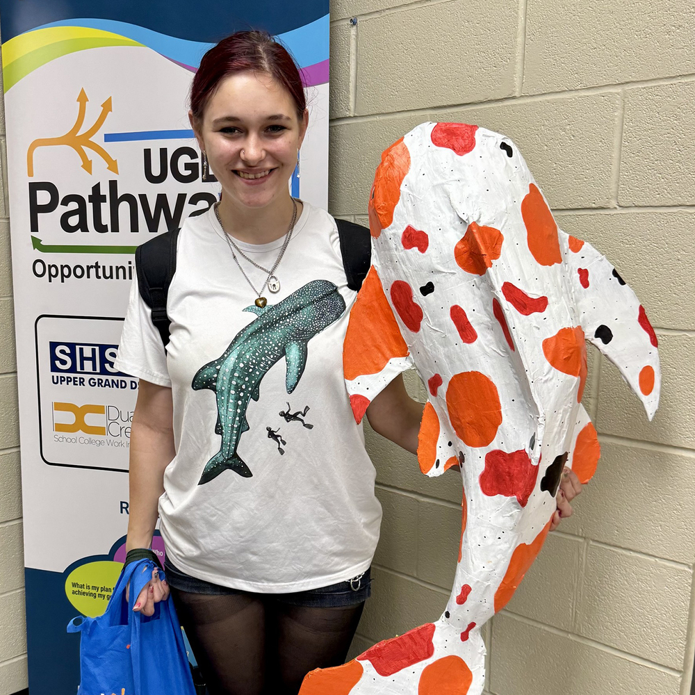 A student holds a koi fish sculpture made from recycled materials.