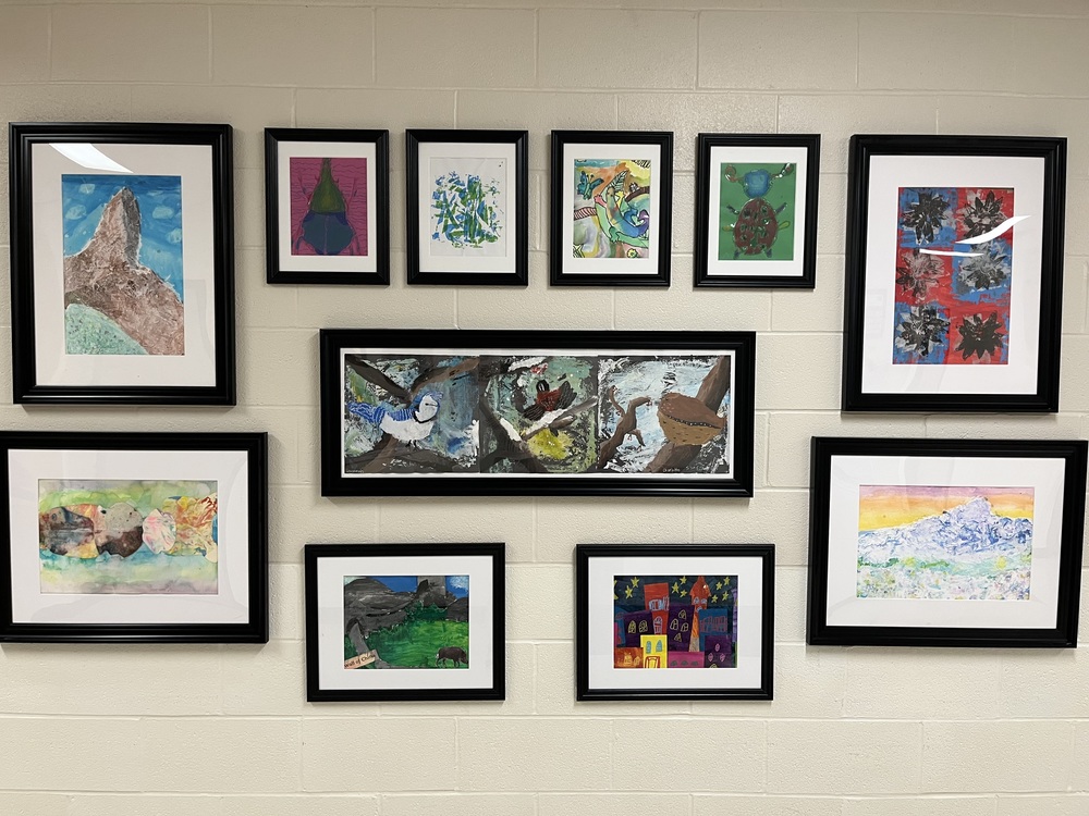 Art gallery wall of various works of student work in paint, chalk. 