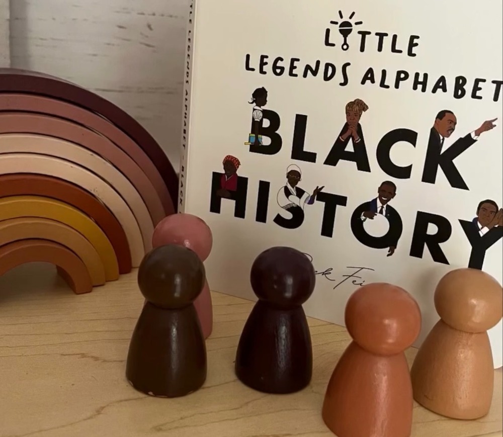 A wooden rainbow and wooden dolls in multiple flesh tone colours and a book about black history
