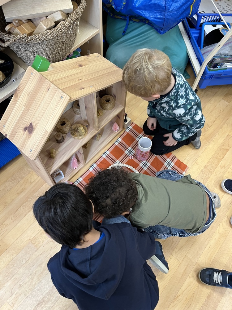Three children playing with a wooden house and gingerbread people.