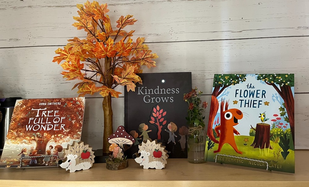 Apple display: hanging banner that reads apple, fall tree model with mushroom and three books about trees, and flowers.