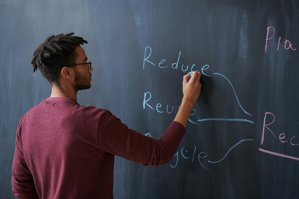 A teacher writes on a blackboard 'reduce, reuse, recycle'