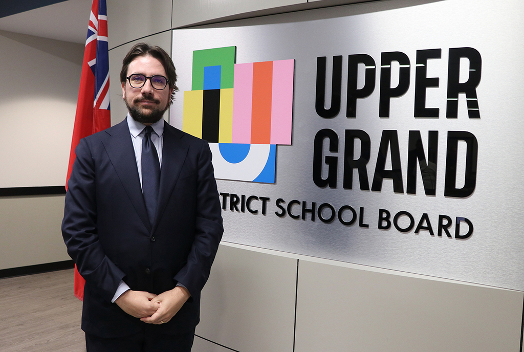 Kyle Reaburn pictured next to the UGDSB logo in the board roomm.
