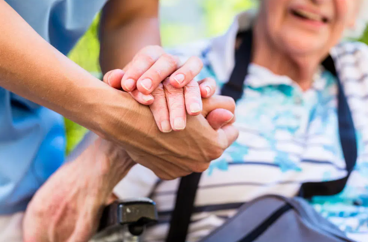 Photograph of a healthcare worker holding the hand of an elderly lady.