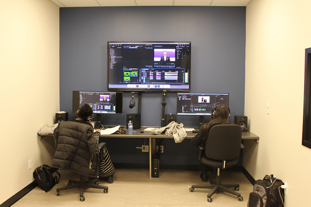 Two students sit at a desk in front of monitors. 