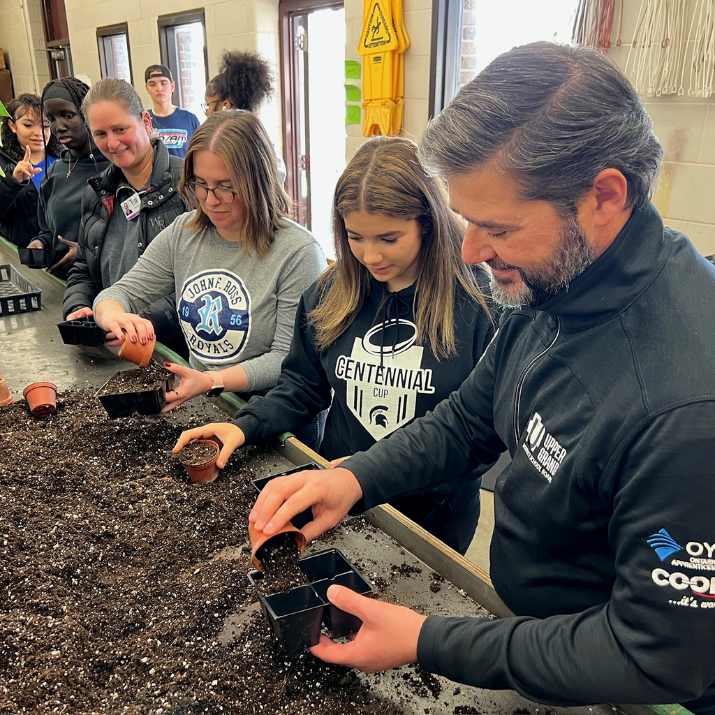 People stand by a table, filling small containers with soil