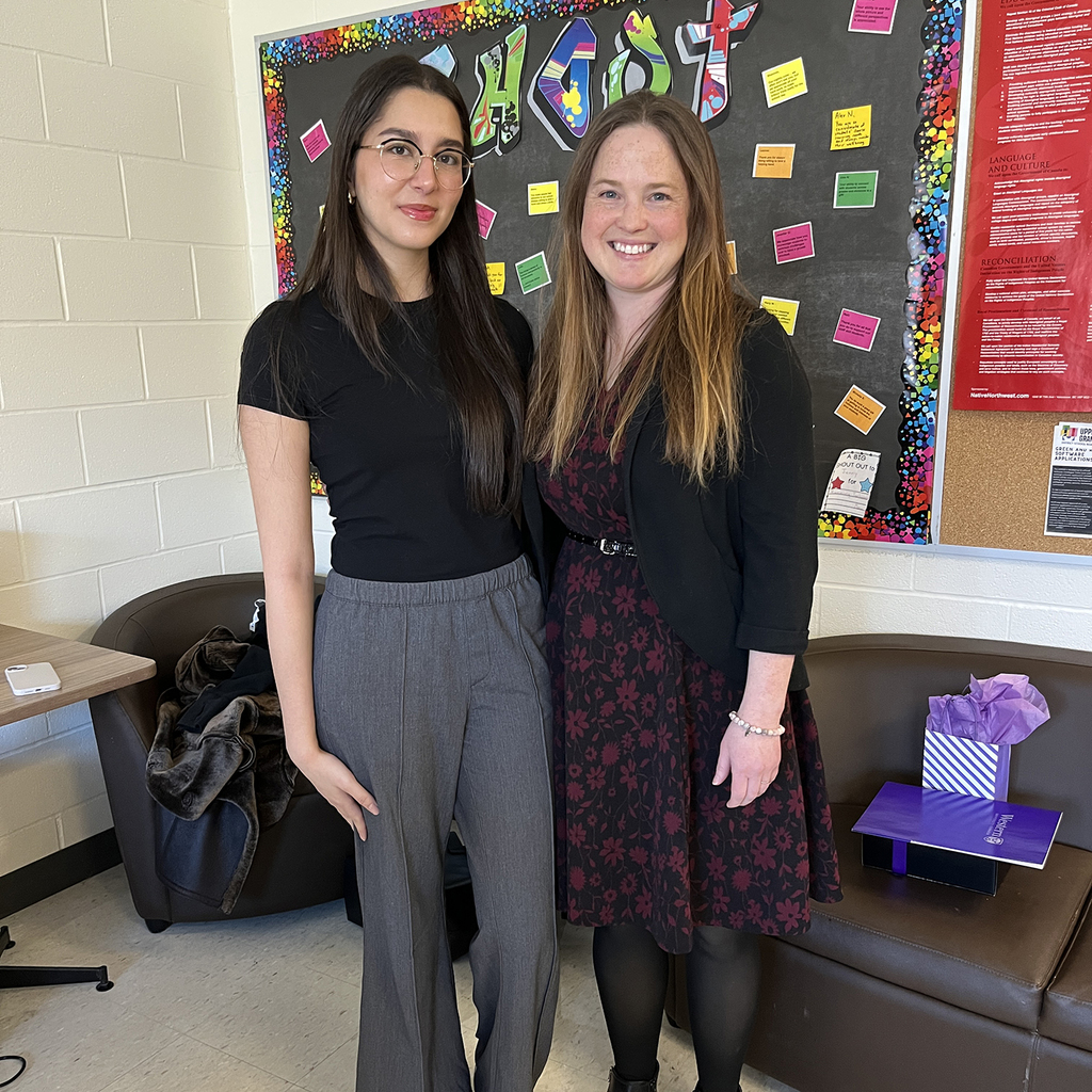 2 people pose for a photograph inside a school staff room