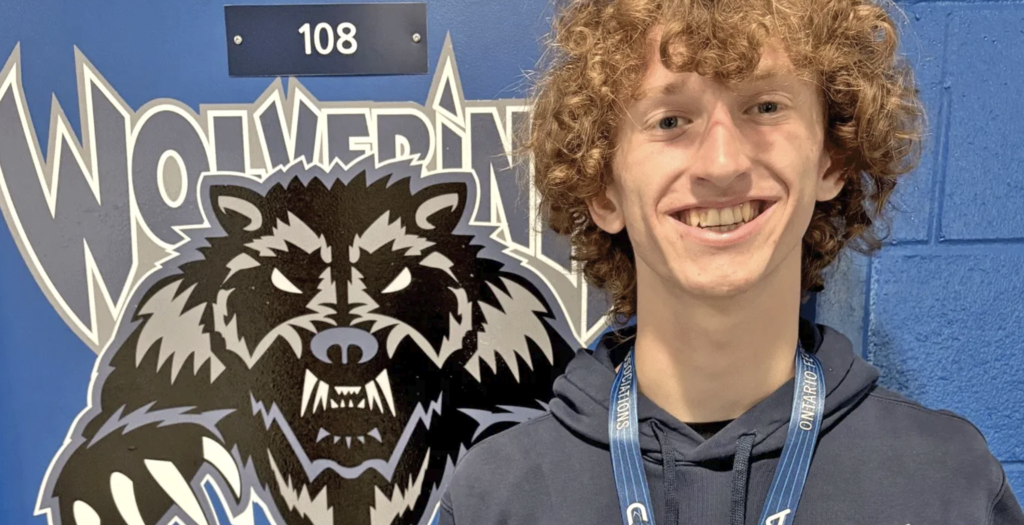 A student stands in front of a Wolverines school logo