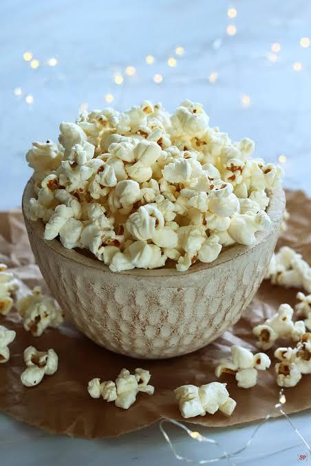 A beige, clay bowl over flowing with big pieces of whte and yellow bits of popcorn.
