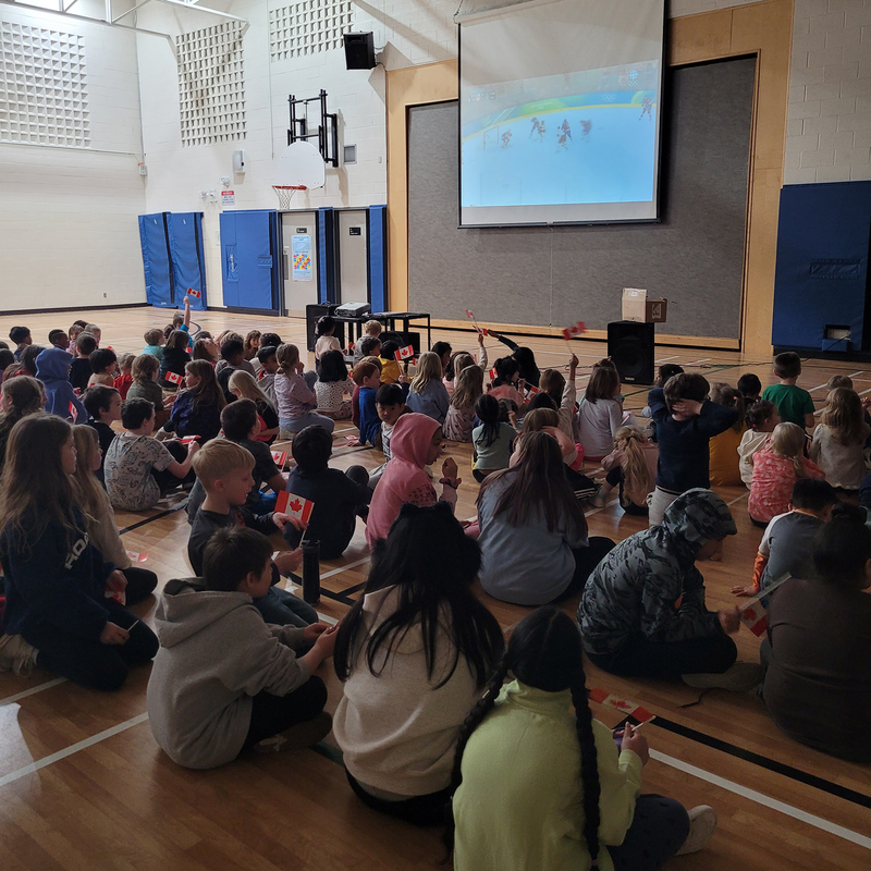 Students sit in a gym watching a hockey game on a screen