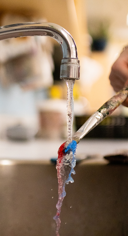 Close up photo of a tap with running water over a paint brush