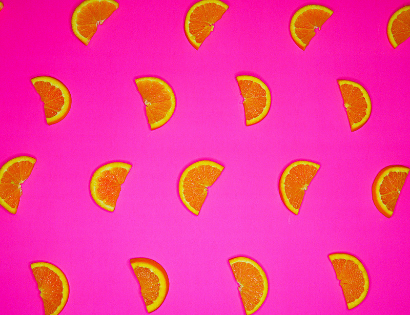 A photograph of halved orange silces on a bright pink background