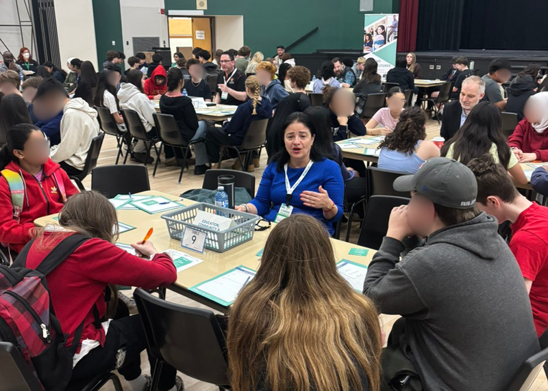 A group of people sit around a table in a large gym space.