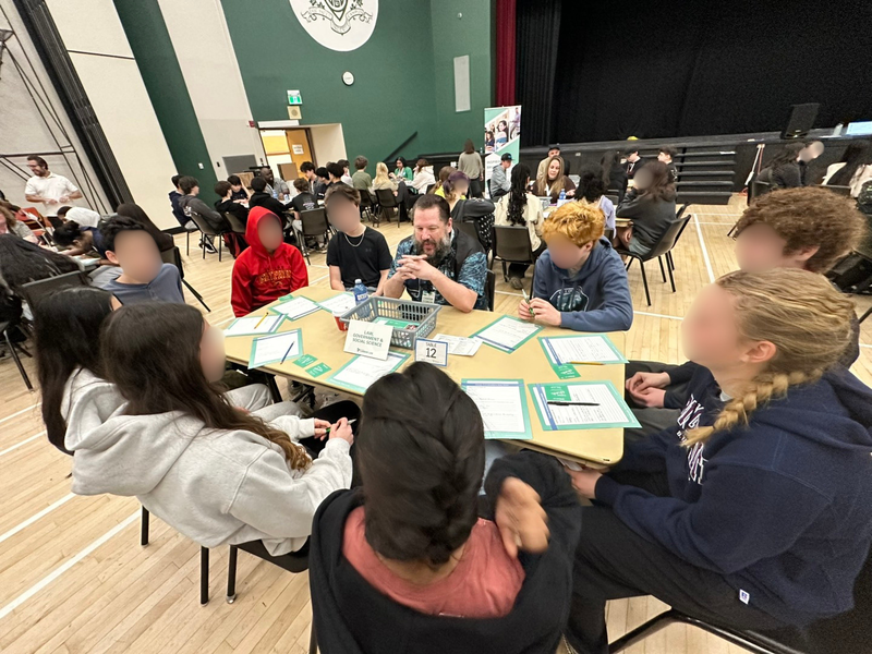 A group of people sit around a table in a large gym space.
