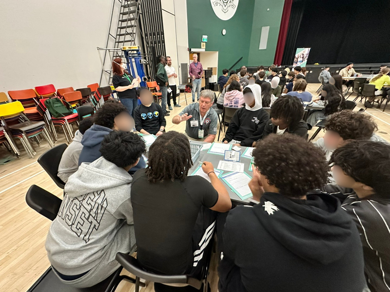 A group of people sit around a table in a large gym space.