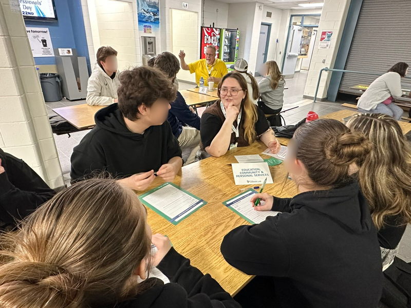 A group of people sit around a table in a large gym space.