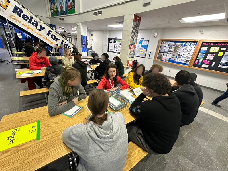 A group of people sit around a table in a large gym space.
