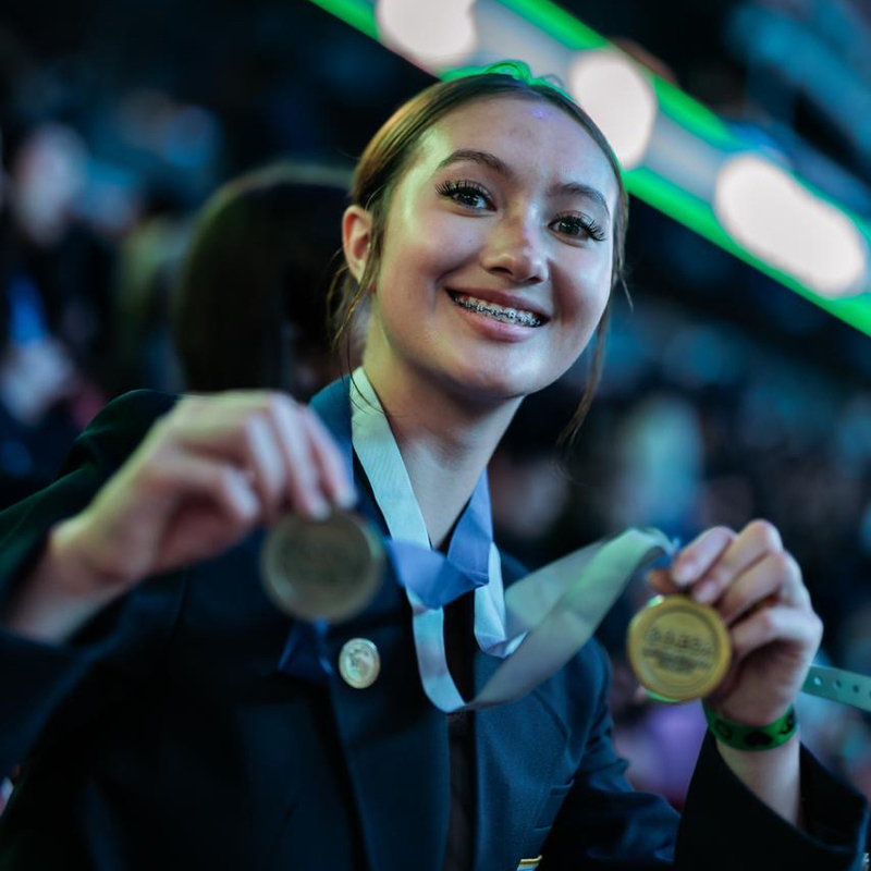 A student smiles for the camera while holding up two medals